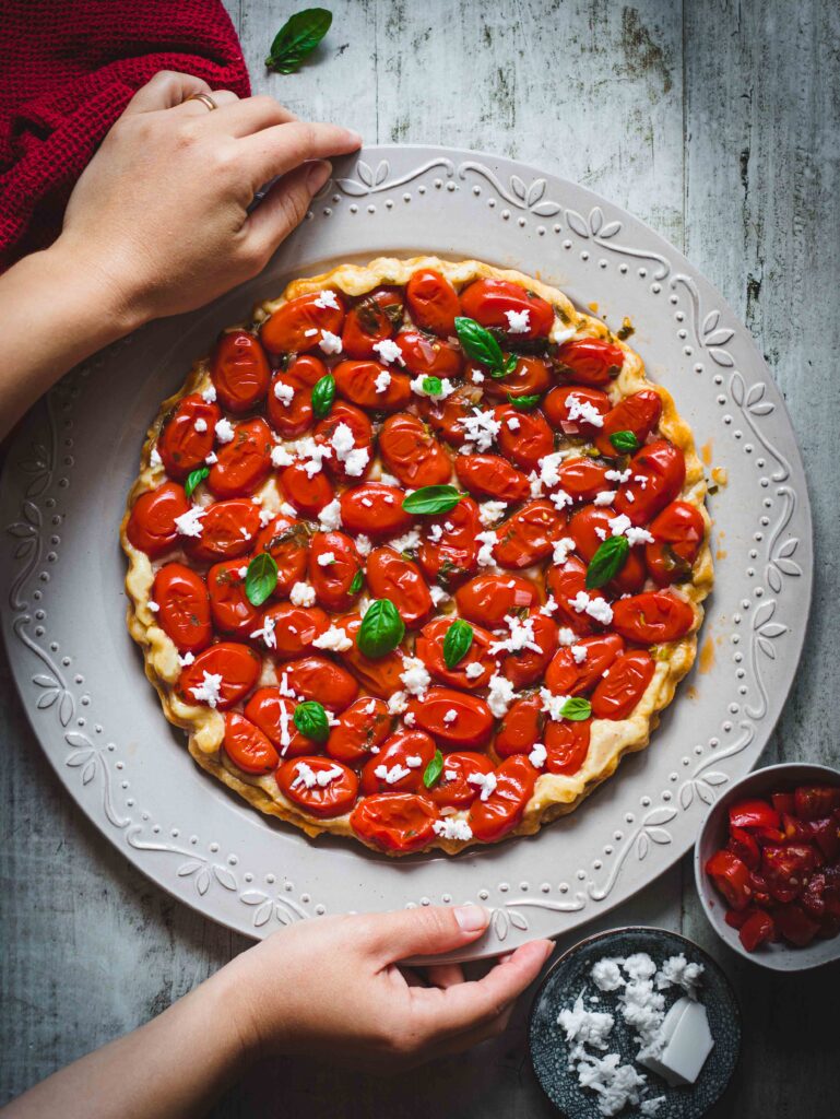 Tarte Tatin con pomodorini e feta in un piatto rotondo bianco su tavolo di legno