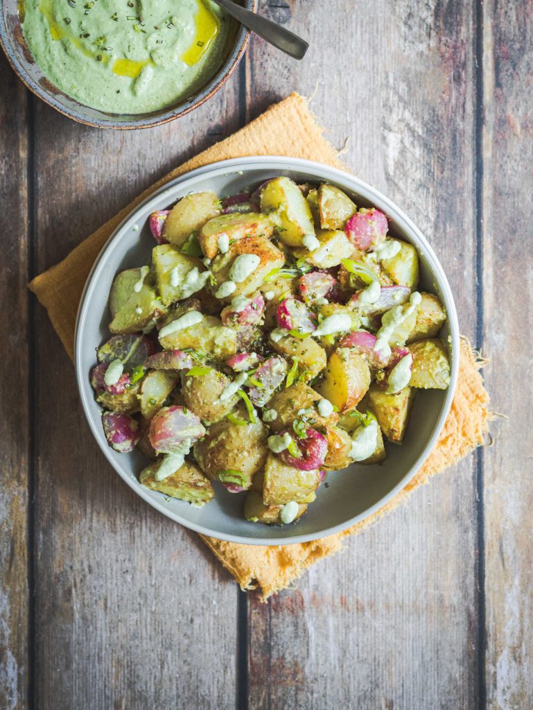 Patate e ravanelli arrosto con salsa ranch al basilico in piatto bianco su legno